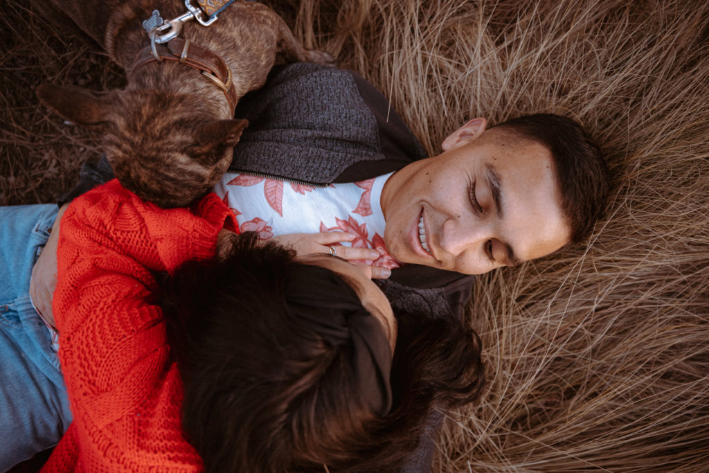 Couple lying down in dried grass with their dog