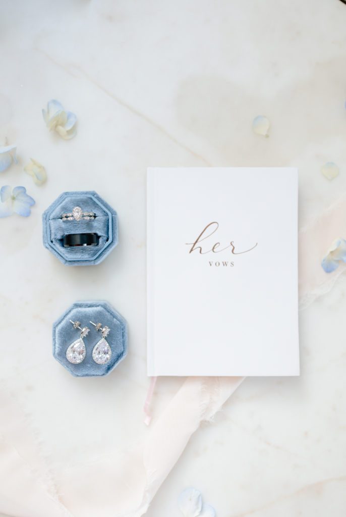 marble backdrop elegant flat lay with vow book, rings, blue ring box and ribbon