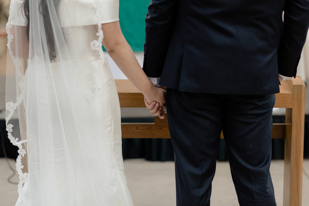 bride and groom hold hands at catholic wedding ceremony